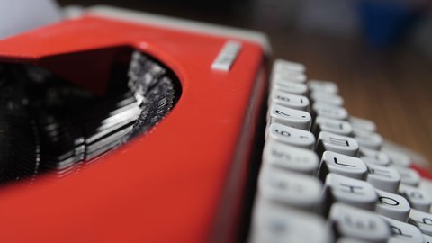 Men's fingers press the buttons on a vintage typewriter. The case is red. Close-up of the keyboard.