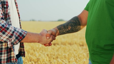 Farmer and agronomist shaking hands after agreement standing in ripe wheat field. Landlord and rancher negotiate on agriculture business contract with handshake. Harvesting season. Global food chain.