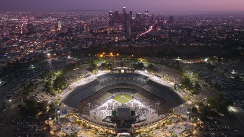 Flyover above Dodgers Stadium illuminated at night. Aerial topdown panorama 4K aerial. Los Angeles city buildings skyline downtown at cinematic pink sunset. Dodgers Stadium, Los Angeles June 2022