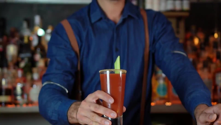 Bartender serves cocktail based on tomato juice Bloody Mary, close-up of hand and cocktail on wooden bar and unfocused background behind, healthy nightlife concept Royalty-Free Stock Footage #1091724823