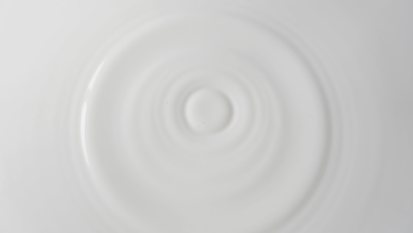Drops of milk drip from top to center on a solid surface of milk close-up. Background of milk with falling drops. 4k raw slow motion video with speed ramp effect. Filmed on high speed cinema camera. | Shutterstock HD Video #1091732103