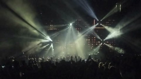 Concert of popular rock band. Professional light equipment on stage. Silhouettes of applauding people enjoying music in concert hall, flashing illumination show, party atmosphere. Famous singer event
