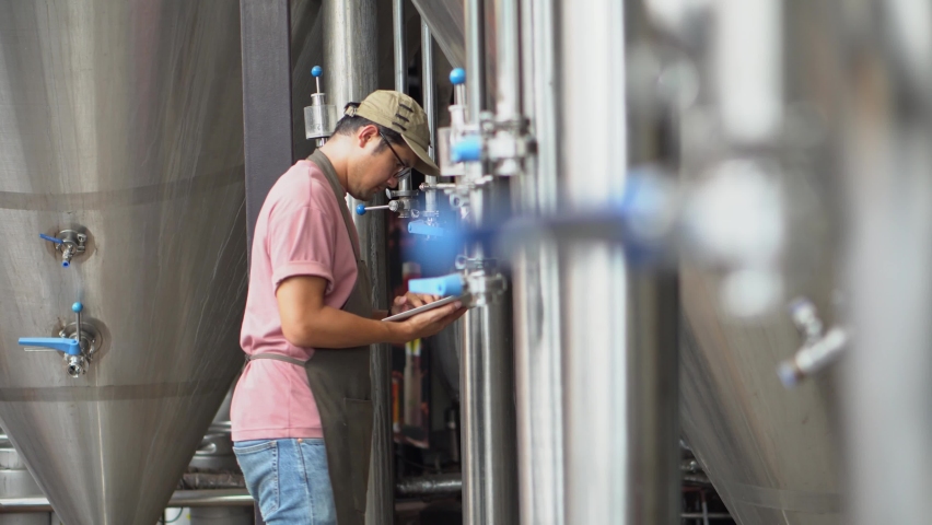Asia male brewery worker with digital tablet in hands setting parameters on storage tank producing beer at factory. | Shutterstock HD Video #1091736089