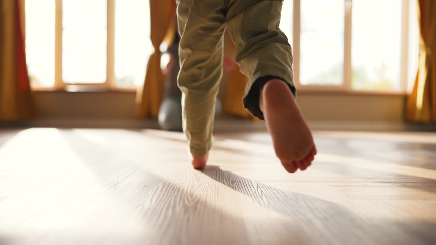 Baby takes first step on floor to his mother with bare feet.Son and mother at home feet on floor.Happy boy barefoot on laminate.Baby foot on wooden floor.Child is learning to walk.Happy family concept