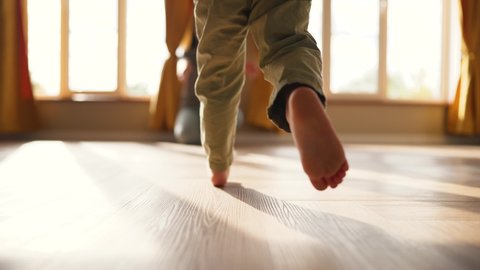 Baby takes first step on floor to his mother with bare feet.Son and mother at home feet on floor.Happy boy barefoot on laminate.Baby foot on wooden floor.Child is learning to walk.Happy family concept ஸ்டாக் வீடியோ