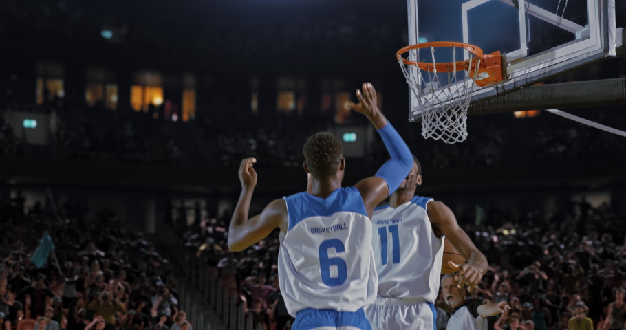 Basketball player throwing the ball into the hoop in a jump and scoring points. Opposite team player blocking. Players celebrating. 3d made basketball stadium with animated crowd.