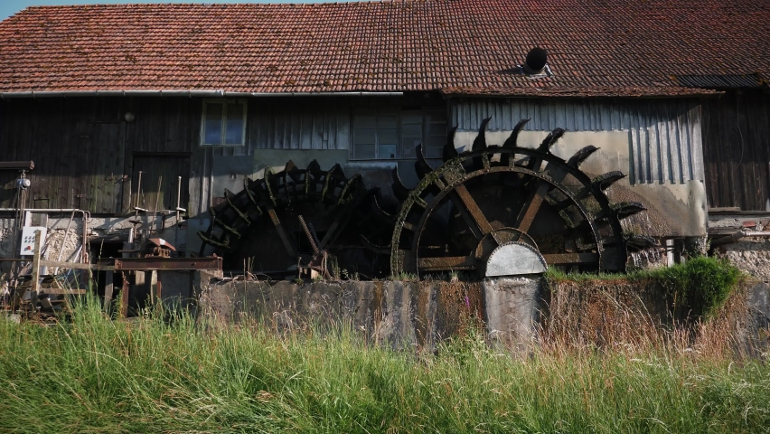 Wooden water mill with big spinning wheels, turning under stream of water