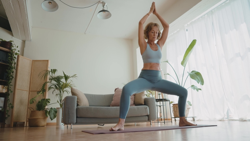 Cinematic storytelling video of a senior old woman practicing yoga and stretching fitness at home. Representation of healthy lifestyle and leisure activities during seniority and the third age | Shutterstock HD Video #1091740881