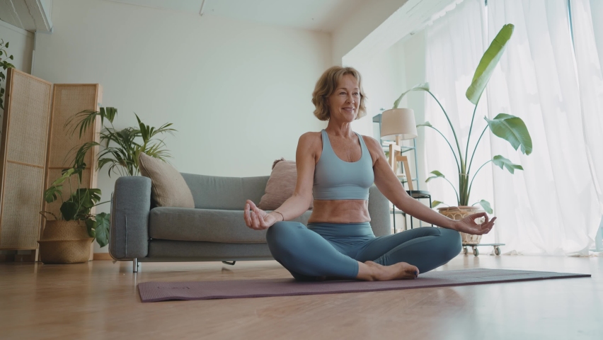 Cinematic storytelling video of a senior old woman practicing yoga and stretching fitness at home. Representation of healthy lifestyle and leisure activities during seniority and the third age | Shutterstock HD Video #1091740887