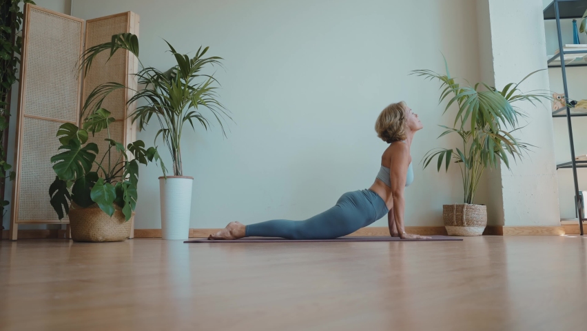 Cinematic storytelling video of a senior old woman practicing yoga and stretching fitness at home. Representation of healthy lifestyle and leisure activities during seniority and the third age | Shutterstock HD Video #1091740901