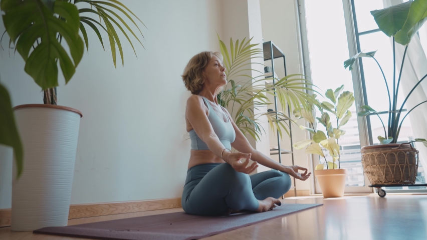 Cinematic storytelling video of a senior old woman practicing yoga and stretching fitness at home. Representation of healthy lifestyle and leisure activities during seniority and the third age | Shutterstock HD Video #1091740907