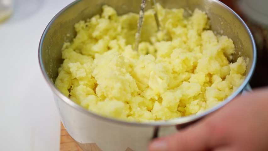 a female hand mashes boiled potatoes with a pusher and adds milk to it, mixes, making mashed potatoes