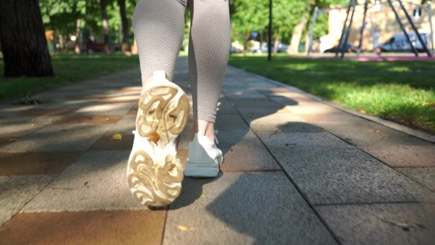 The legs of a young woman in white sneakers run along the path in the park | Shutterstock HD Video #1091741617