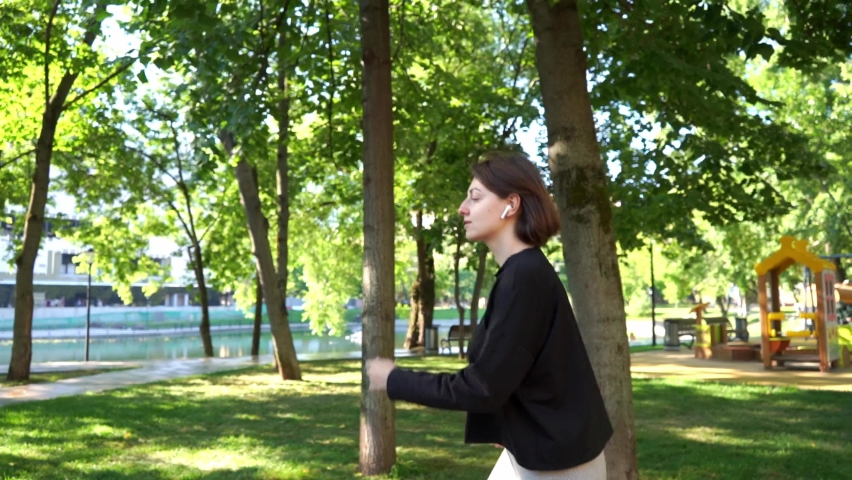 A young brunette woman in wireless headphones on a run in a summer park in the city. Side view | Shutterstock HD Video #1091741625
