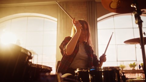 Portrait of a Young Female Playing Drums During a Band Rehearsal in a Loft Studio with Warm Sunlight at Daytime. Drummer Girl Practising Before a Live Concert on Stage. Static Shot.