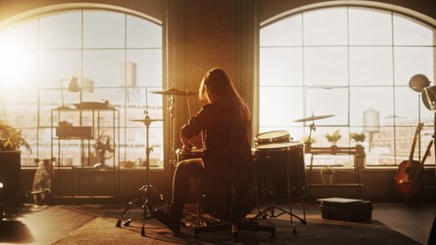 Female or Male with Long Hair Sitting with Their Back to Camera, Playing Drums During a Band Rehearsal in a Loft Studio. Heavy Metal Drummer Practising a Drum Solo Alone.