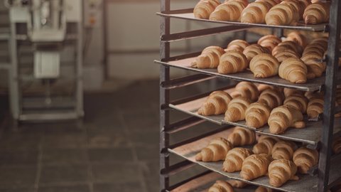 Freshly baked fragrant croissants with a ruddy appetizing golden crust. Croissants stand on metal shelves in the bakery. Slow movement of the cameras from the bottom up. Food Industry. Close up