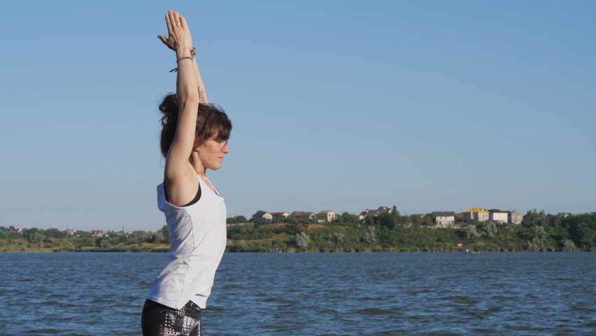 a young woman practices yoga on a pier by the lake. A woman in black leggings practices yoga. slow motion 4K