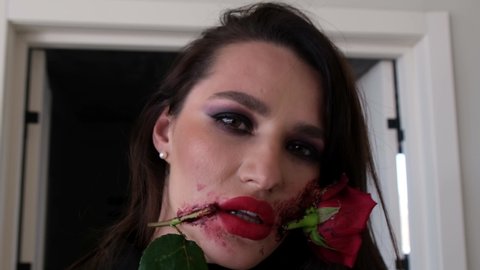 Beautiful young brunette woman with makeup for Halloween, rose flower in her mouth. 
