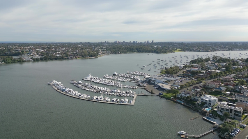 Luxury ocean village marina at San Souci and Taren Point, Sydney Australia. Cloudy and blue skies over the sailing boats, motorboats, pontoons. Expensive boat moorings. Aerial drone orbit shot.