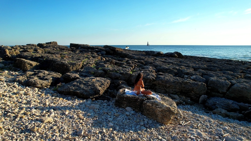 Circling around a pretty brunette sitting on the rocks looking the ocean at Cascais,Portugal