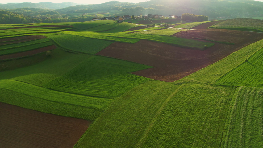 AERIAL: Gorgeous hilly rural countryside with small villages and farming land. Picturesque agricultural landscape with lovely pattern of pastures and farm fields. Idyllic landscape in afternoon light. Royalty-Free Stock Footage #1091751691