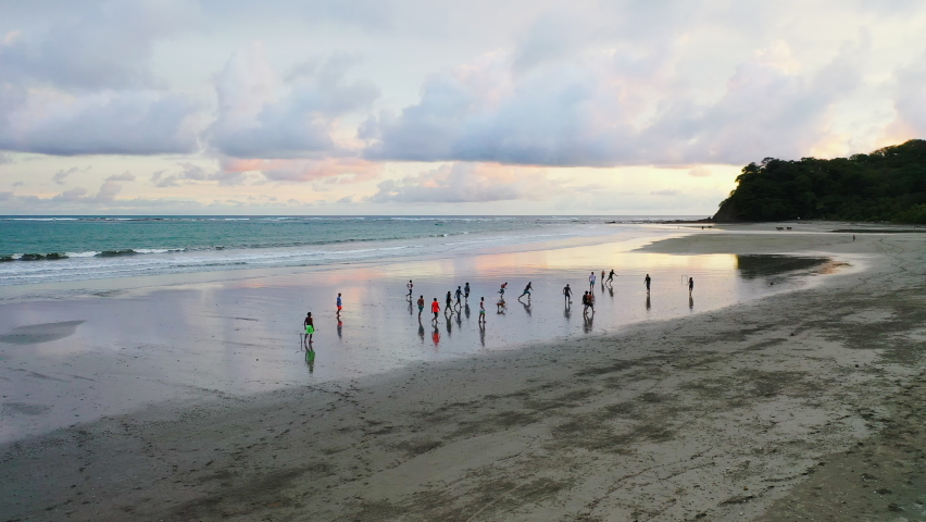 A drone flies over a group of football players at sunset on a Costa Rican beach