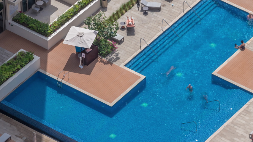 Rooftop swimming pool viewed from above timelapse, Aerial top view with people swimming and relaxing under umbrellas. Moving shadows