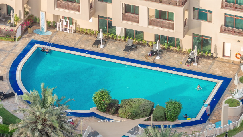 Swimming pool with blue water viewed from above timelapse, Aerial top view in Greens district. People swimming and relaxing on a chaise longue. Dubai, UAE