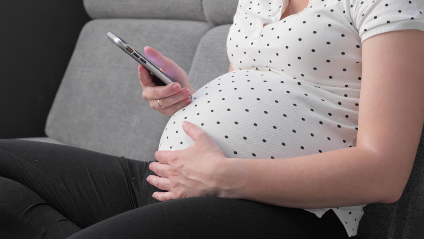 Pregnant woman using mobile phone while sitting on sofa at home. Unrecognized pregnant female with smartphone. - Powered by Shutterstock - Get 15% off with code: PIKWIZARD15