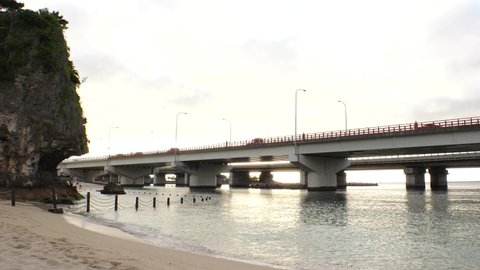 NAHA, OKINAWA, JAPAN - AUG 2021 : View of Naminoue beach (Ocean or sea) and road traffic in sunset time. Wide view, time lapse shot, dusk to night. Summer holiday, vacation and resort concept shot.