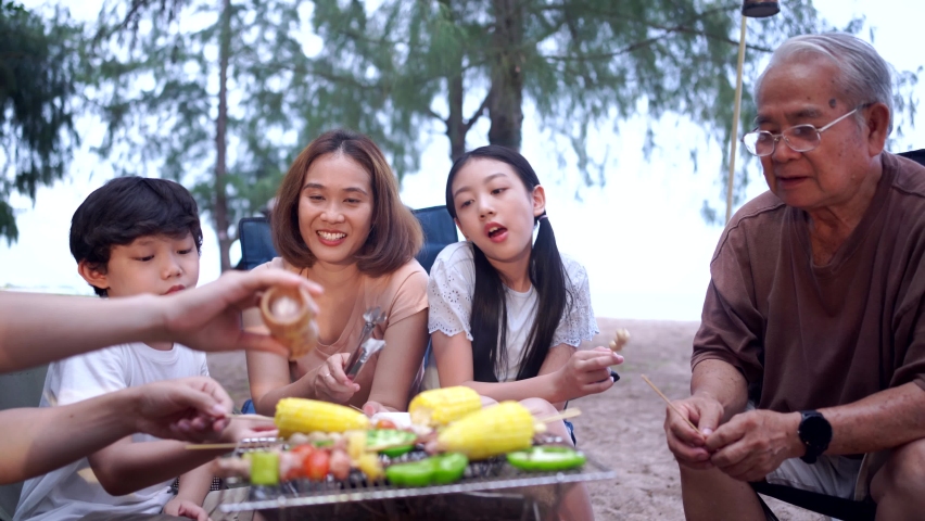 Happy Asian family having barbecue together. Cooking grilled bbq for dinner during camping on summer beach. | Shutterstock HD Video #1091766113