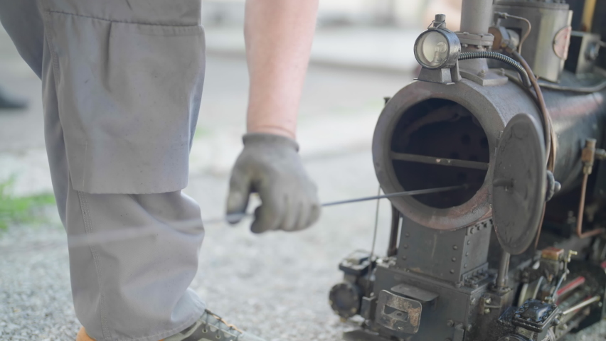 Person clean steam train engine with long brush stick 4K