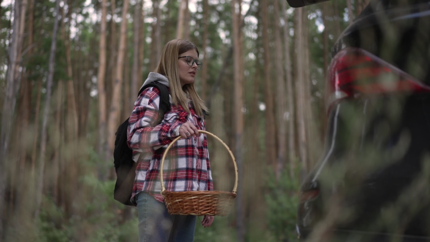 Side view confident woman putting wicker basket and backpack in car closing trunk in slow motion. Medium shot portrait of Caucasian traveler at the end of journey in forest outdoors | Shutterstock HD Video #1091769203
