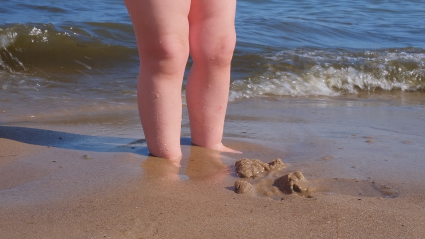 Caucasian Baby Standing at Sea Shore Sinking Feet in Wet Sand Overflown with Waves of Water | Shutterstock HD Video #1091769651