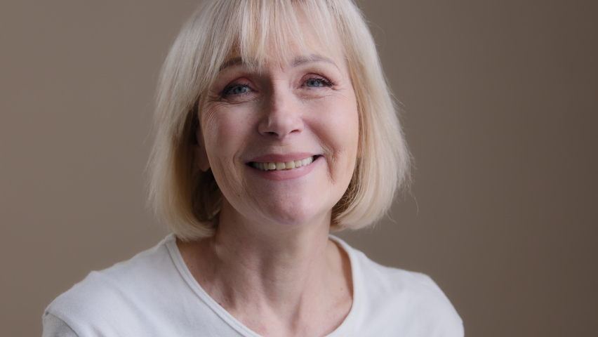 Happy mature middle-aged blonde smiling caucasian 60s woman looking at camera posing in studio portrait, cheerful older grey-haired female granny in white t-shirt, healthy carefree senior retired lady Royalty-Free Stock Footage #1091770657
