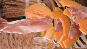 Italian prosciutto crudo with melons. Slices of traditional ham wrapped around melons. Tasty appetizer. Food background. Close up. Snack for wine for an aperitif. Vertical video, for social networks