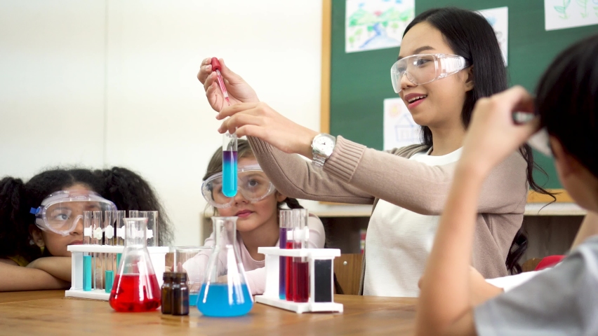 Young woman mixing liquids in test tube with multiethnic children watching, learning about science, chemistry. Asian school teacher and students in science class Royalty-Free Stock Footage #1091775123