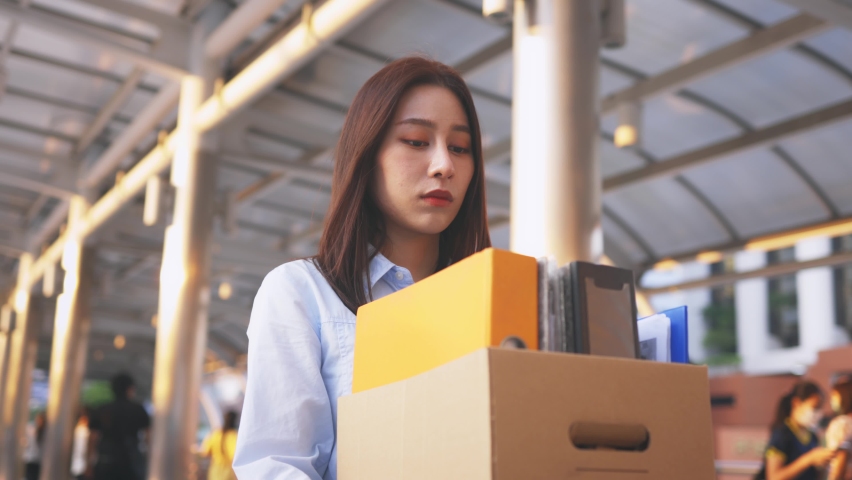 Portrait of young Asian woman walking and holding box of items after being laid off from job due to recession and economic stress in industry Royalty-Free Stock Footage #1091775131