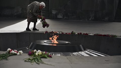 Yerevan, Armenia - 14 Apr, 2022: Old woman putting flowers near the "eternal fire" on the territory of The Armenian Genocide Memorial complex in Yerevan. Armenia