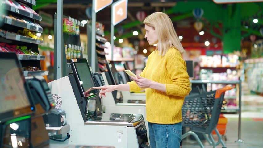 Female buyer using a self-service cashier checkout in a supermarket. Customer scanning produce items using at grocery store self serve cash register. cashier terminal woman pay for products online | Shutterstock HD Video #1091778701