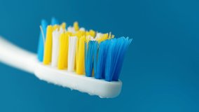 White toothpaste with a beautiful curl at the end squeezed out of a tube on a toothbrush close-up on a blue background. 4k raw macro video.