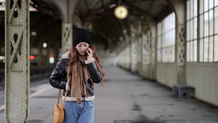 A beautiful girl is talking sadly on a mobile phone. Waiting for the train at the train station.