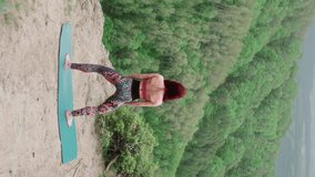 Vertical Video Athletic woman practices yoga on top mountain against backdrop beautiful green valley. Slim girl goes in for sports outdoors. Healthy lifestyle. Meditation and balance concept. Asana.