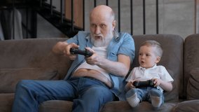 Happy family grandfather plays video game with his boy grandson at home. Mature man and boy use game joysticks. Older man wins in computer game. Happy grandfather celebrate victory.