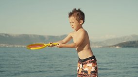 Close-up slow motion video of a baby boy with a racket playing tennis. A child on vacation on the beach plays games and actively relaxes. High quality 4k footage