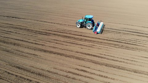 Aerial view of a farmer in tractor seeding corn. Drone shot of planting agricultural crops at field