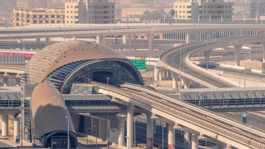 Futuristic building of Dubai metro station and luxury skyscrapers behind in Dubai Marina aerial timelapse. Traffic on Sheikh Zayed road highway with power lines on a background, United Arab Emirates