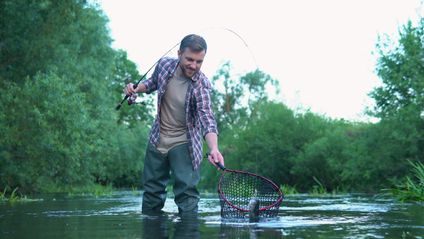 Fisherman with fishing rod on the river. Fly fishing for trout. Summer holidays and people concept. Brown trout fish. Trout on a hook. Holding trout fish