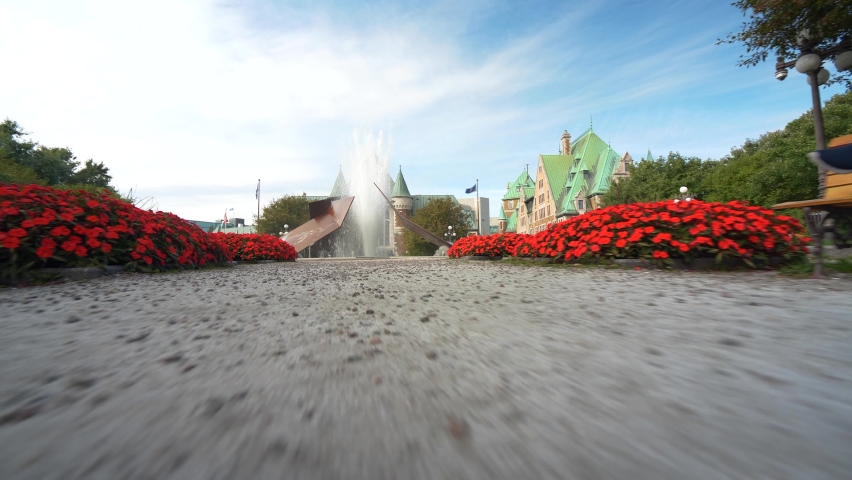 Ground level view walking towards the Eclatement II, or Bursting II, water fountain sculpture at Jean Pelletier park with architecture of Old Quebec.